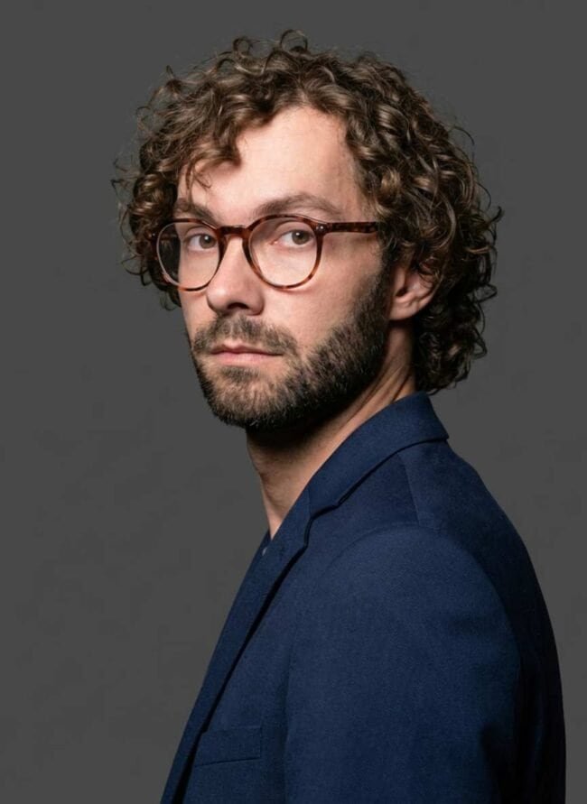 1. Portrait of a man with curly hair and glasses in a professional studio setting.